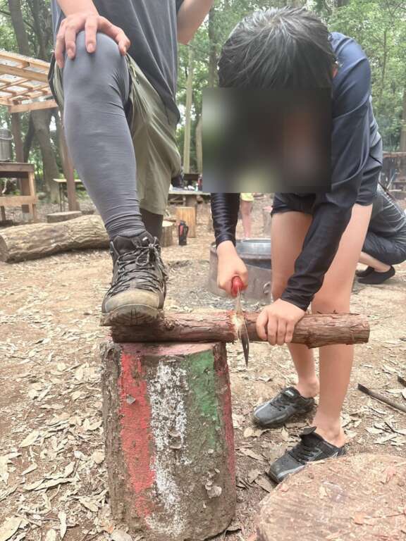 ノコギリで薪を切る小学生